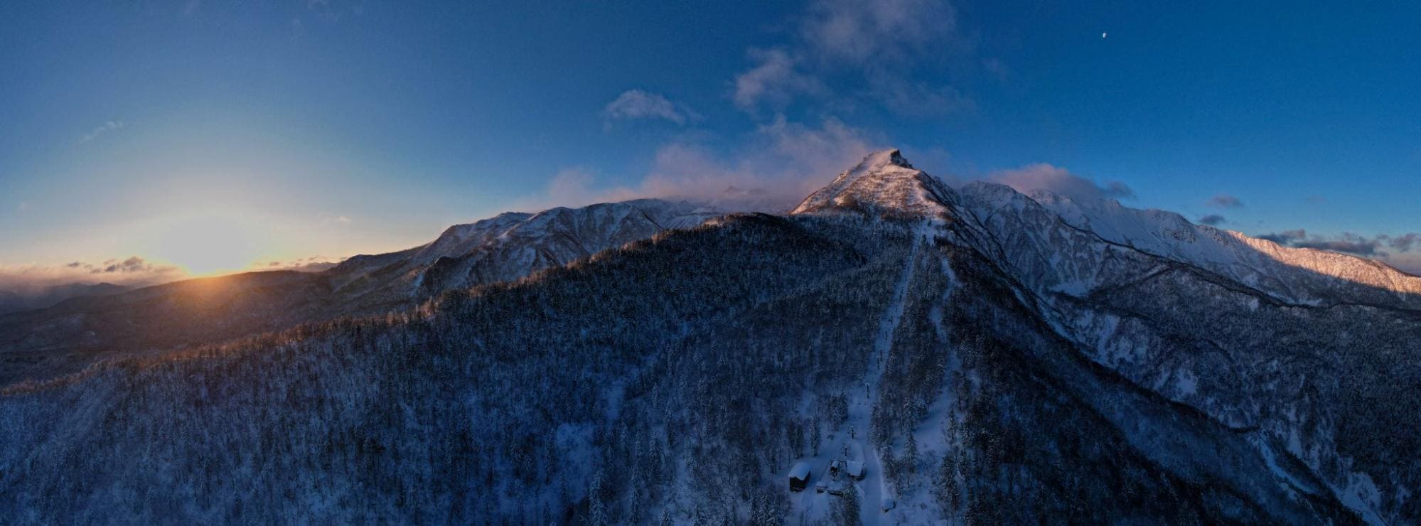 Drone shot of snow-covered Sandan Yama and Mount Tokachi, with volcanic smoke rising from the peaks against a clear sky.